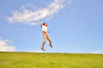 芝生広場でジャンプする女の子（青空）