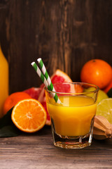Glass of fresh homemade orange juice with pile of fruits over grunge wooden background. Selective focus