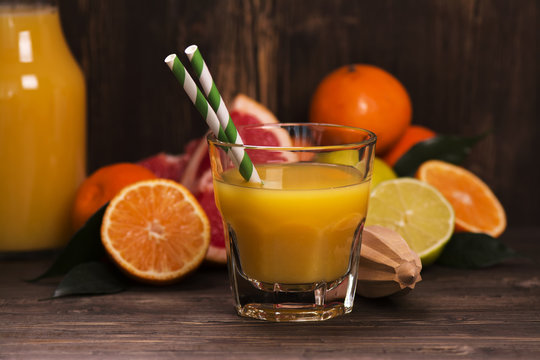 Glass of fresh homemade orange juice with pile of fruits over grunge wooden background. Selective focus