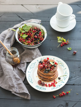 Breakfast set. Buckwheat pancakes with fresh berries and honey on rustic plate over black wooden table.