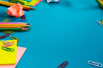 Office table desk with set of colorful supplies, white blank note pad, cup, pen, pc, crumpled paper, flower on blue background. Top view and copy space for text