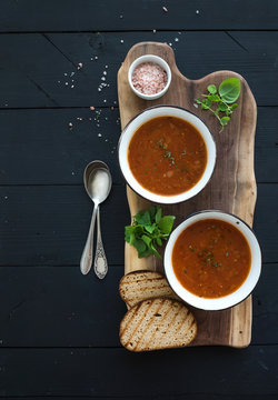 Roasted tomato soup with fresh basil, spices and bread in vintage metal bowl on wooden board over black background