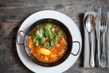 Tasty soup with meat and tomato and cilantro served on a table with instruments