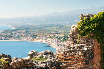Fototapeta na wymiar Section of the upper perimetral arcade of the greek theater of Taormina, Sicily, with a view of Giardini Naxos in the background
