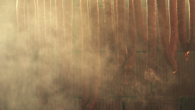 Homemade smoked sausages, cured pork meat, food preparation process in smokehouse.