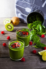Fresh green smoothie sprinkled with chia seeds and goji berries in the background fruits and vegetables on wooden table.