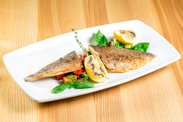 Tasty baked fish with grilled vegetables on  plate on wooden table close-up