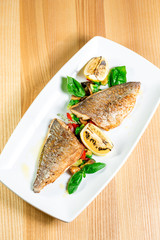 Tasty baked fish with grilled vegetables on  plate on wooden table close-up