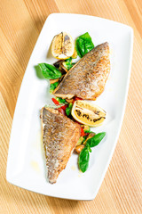 Tasty baked fish with grilled vegetables on  plate on wooden table close-up