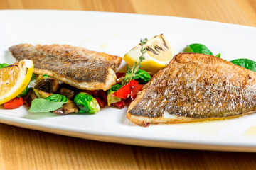 Tasty baked fish with grilled vegetables on  plate on wooden table close-up