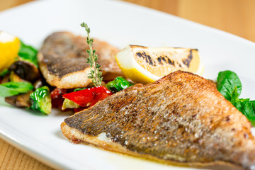 Tasty baked fish with grilled vegetables on  plate on wooden table close-up