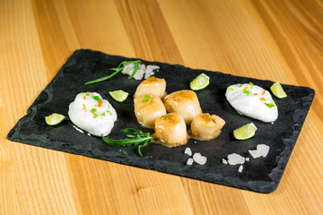 Studio close up of seared scallops, garnished with greens and sauce