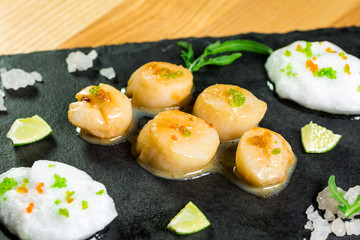 Studio close up of seared scallops, garnished with greens and sauce