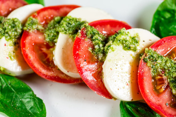 Caprese salad with mozzarella, tomato, basil and balsamic vinegar arranged on white plate