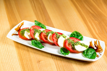 Caprese salad with mozzarella, tomato, basil and balsamic vinegar arranged on white plate