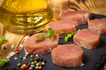 Pieces of raw meat on a plate of slate herbs spices and olive oi