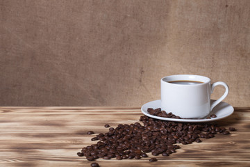 Coffee beans and coffee in white cup on wooden table opposite a