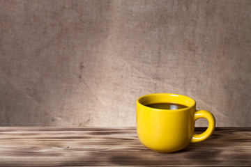 Coffee in cup on wooden table opposite a defocused burlap backgr