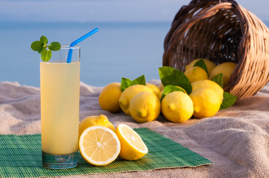 Glass of fresh lemon juice and a full wicker basket with blue sea in the background