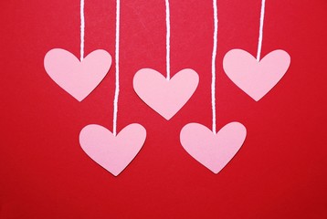 Fototapeta na wymiar Hearts hanging by string on a red background, can be used for a Valentine's Day or Mother's Day project