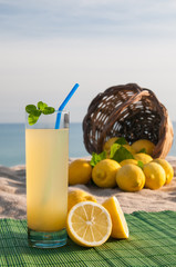 Glass of fresh lemon juice and a full wicker basket with blue sea in the background