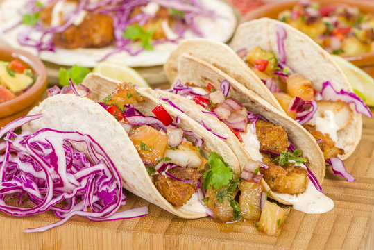 Baja Fish Tacos - Soft shell tacos filled with seasoned fried white fish served with red cabbage, pineapple salsa, chunky guacamole and creamy Baja style sauce.
