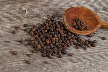 whole black pepper on wooden spoon