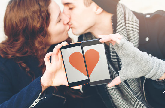 Young couple in love, with cell phones with a heart shape image, kissing