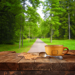front image of coffee cup over wooden table in front of forest background
