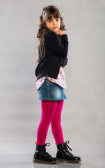 Smiling little girl standing on the gray background. Positive emotional little girl with long healthy hair and a sweet smile posing at the camera on a gray background