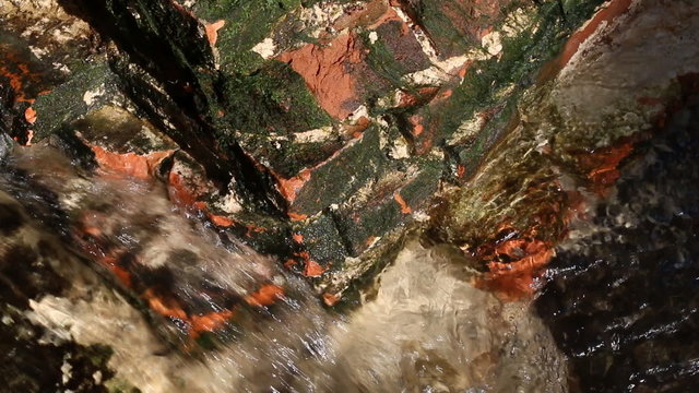 Flow of a stream near old destroyed red brick wall.