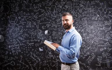 Teacher with book against big blackboard with symbols and formul