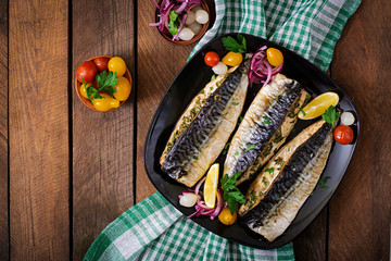 Baked mackerel with herbs and garnished with lemon and pickled vegetables. Top view