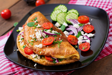 Omelet with tomatoes, parsley and feta cheese on black plate.