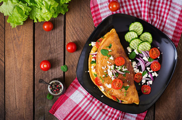 Omelet with tomatoes, parsley and feta cheese on black plate. Top view