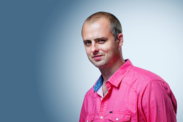 Close up portrait of short-haired brutal man wearing pink shirt on gray background
