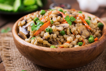 Vegetarian crumbly pearl barley porridge with mushrooms and green peas in a wooden bowl
