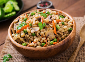 Vegetarian crumbly pearl barley porridge with mushrooms and green peas in a wooden bowl