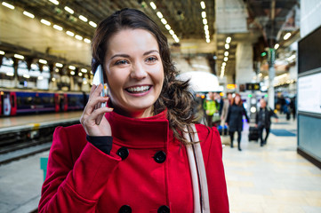 Woman in red coat on train station talking on phone