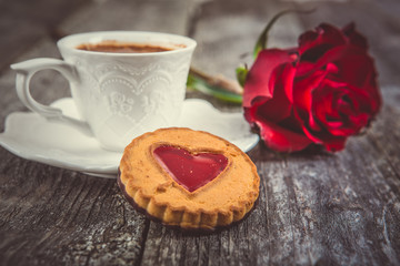 Valentines Day card - Cookies with heart and cup of coffee, red rose at old wooden background.  Instagram colored toning