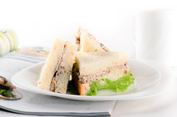 Breakfast of creamy tuna sandwiches with cup of tea and a journa