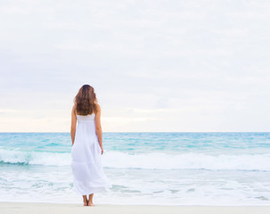 Fototapeta na wymiar Beautiful brunette going to the wavy ocean holding her white dress.
