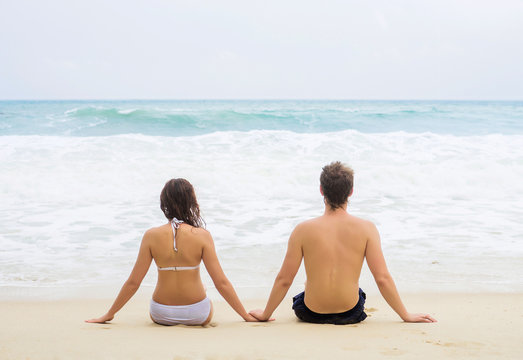 Young couple sitting on the beach. Back view.