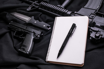 Notepad, pen, gun and knife on black cloth,top view/Notebook for notes with pen and guns with knife on black cloth background