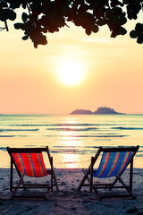 Pair of lounge chairs on sunset at beach.