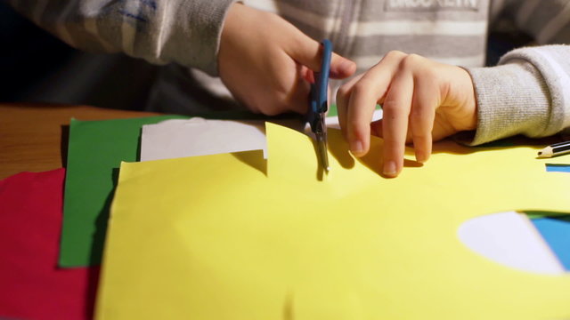 Child using scissors to cut square piece from the paper

