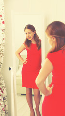 woman in a red dress looks in the mirror