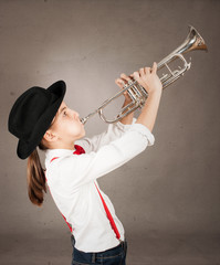 little girl playing trumpet on a gray background