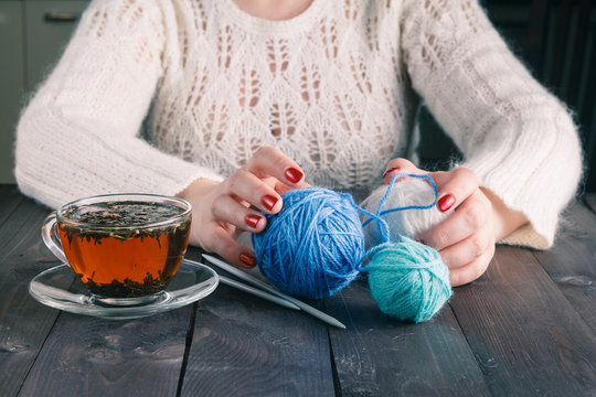 Woman hands with cup of tea and wool yarn balls on a wooden tabl