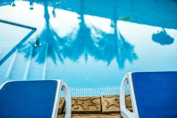 Closeup sunloungers and swimming pool with reflected palms in water 